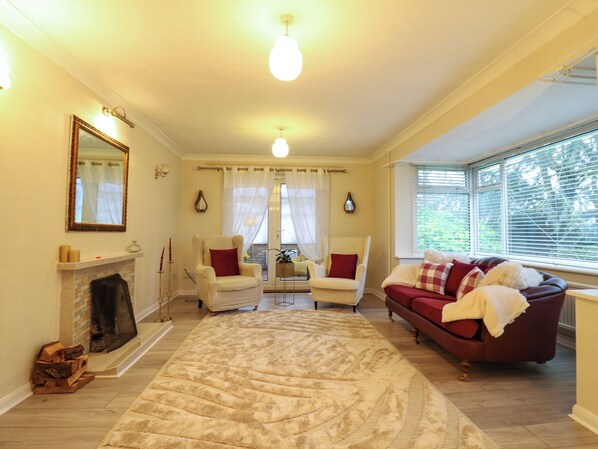 A living room with a fireplace, two armchairs, a sofa, and a large rug.