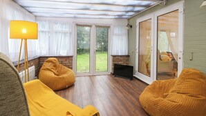 A cozy living room with a fireplace, a large window, and a sliding glass door leading to a garden. - Crown Farm (Wisbech)