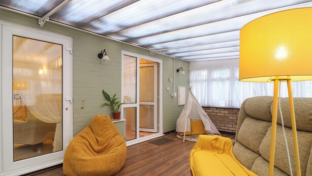 A cozy living room with a wooden floor, a yellow bean bag, a yellow throw blanket, and a yellow floor lamp. - Crown Farm (Wisbech)