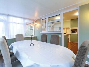 A conference room with a white table, four chairs, a tripod, and a view of a kitchen area.