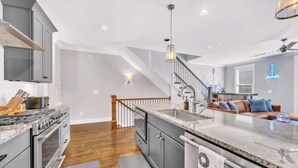 A modern kitchen with grey cabinets, a stainless steel range, and a marble countertop. - Close to DT Game Garage Bar Large Living Room (Nashville)