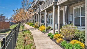 A row of townhouses with balconies, a concrete pathway, and landscaped gardens with yellow and green plants. - Close to DT Game Garage Bar Large Living Room (Nashville)