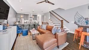 A modern living room with a leather sofa, a coffee table, and a dining area with orange stools. - Close to DT Game Garage Bar Large Living Room (Nashville)