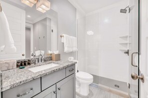 A modern bathroom with a granite countertop, white fixtures, and a glass shower enclosure. - Close to DT Game Garage Bar Large Living Room (Nashville)