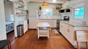 A compact kitchen with white cabinetry, a central island, and a hanging light fixture. - La Palapa whole house at pedestrian beach! Surfside Beach Texas! (Freeport)