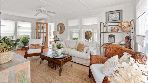 A spacious living room with a white sofa, wicker chairs, a coffee table, and a bookshelf. - Cape Cod Bungalow Walk to Beach Firepit (Yarmouth)