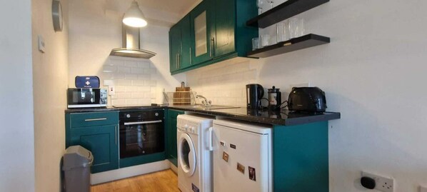 Compact kitchen area with microwave, oven, washing machine, and coffee maker.