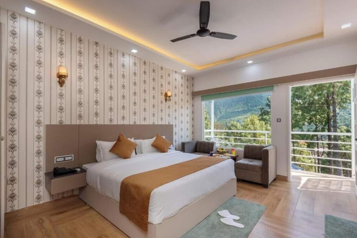 A modern hotel room with a large bed, a sofa, a balcony with a view of the mountains, and a ceiling fan.