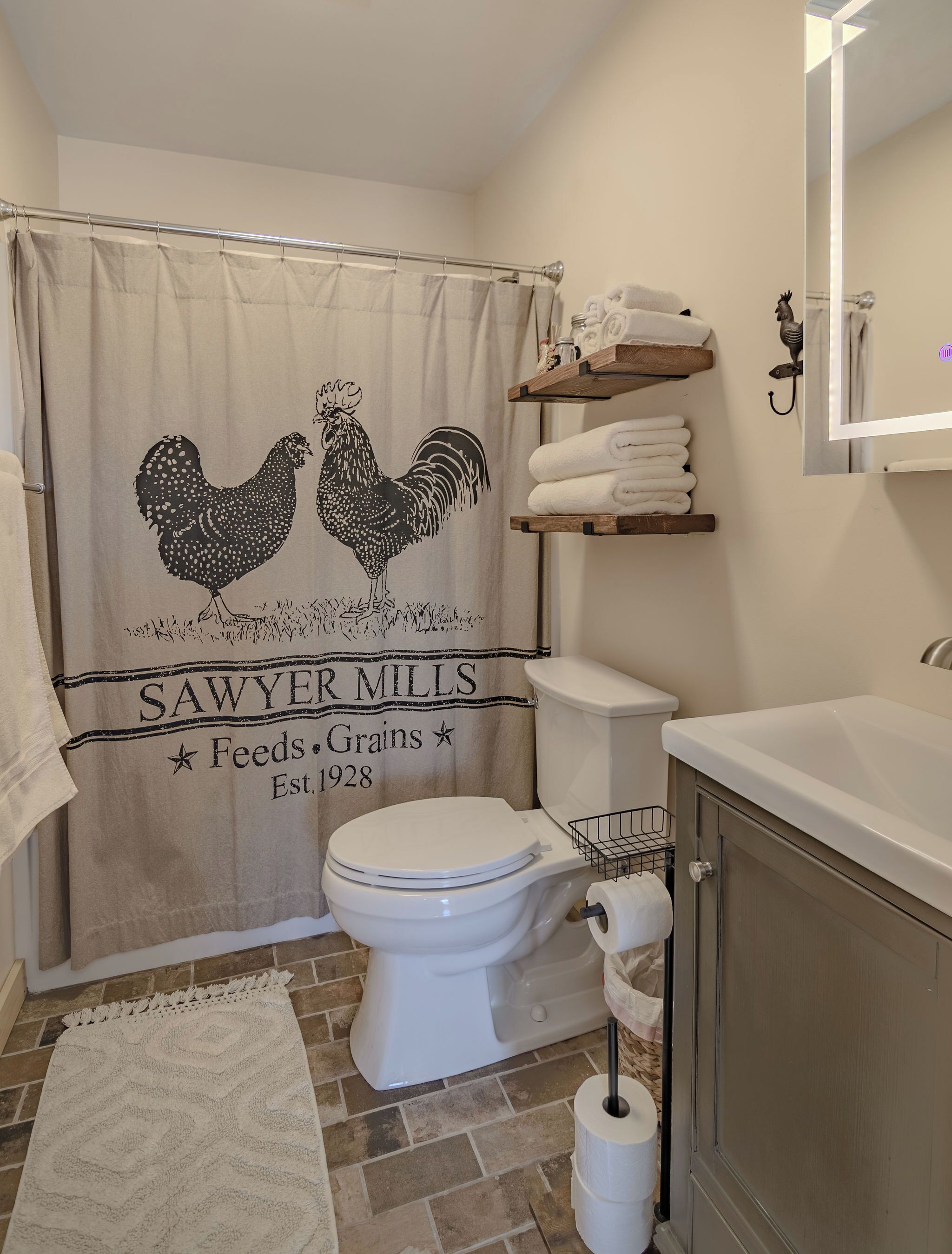 A bathroom with a shower curtain featuring a rooster design, a toilet, a sink, and a towel rack.
