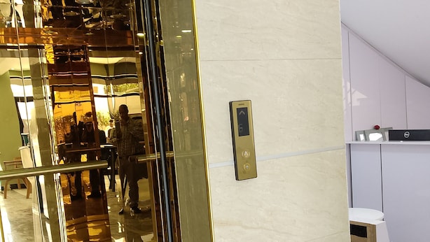 Un espace d’accueil doté d’une porte en verre, d’une enseigne au-dessus et d’un petit panneau de commande pour l’ascenseur.