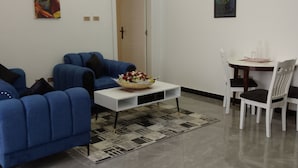Un salon moderne comprenant un canapé, une table basse agrémentée d’un arrangement floral, une table à manger avec des chaises et une porte avec une pancarte.