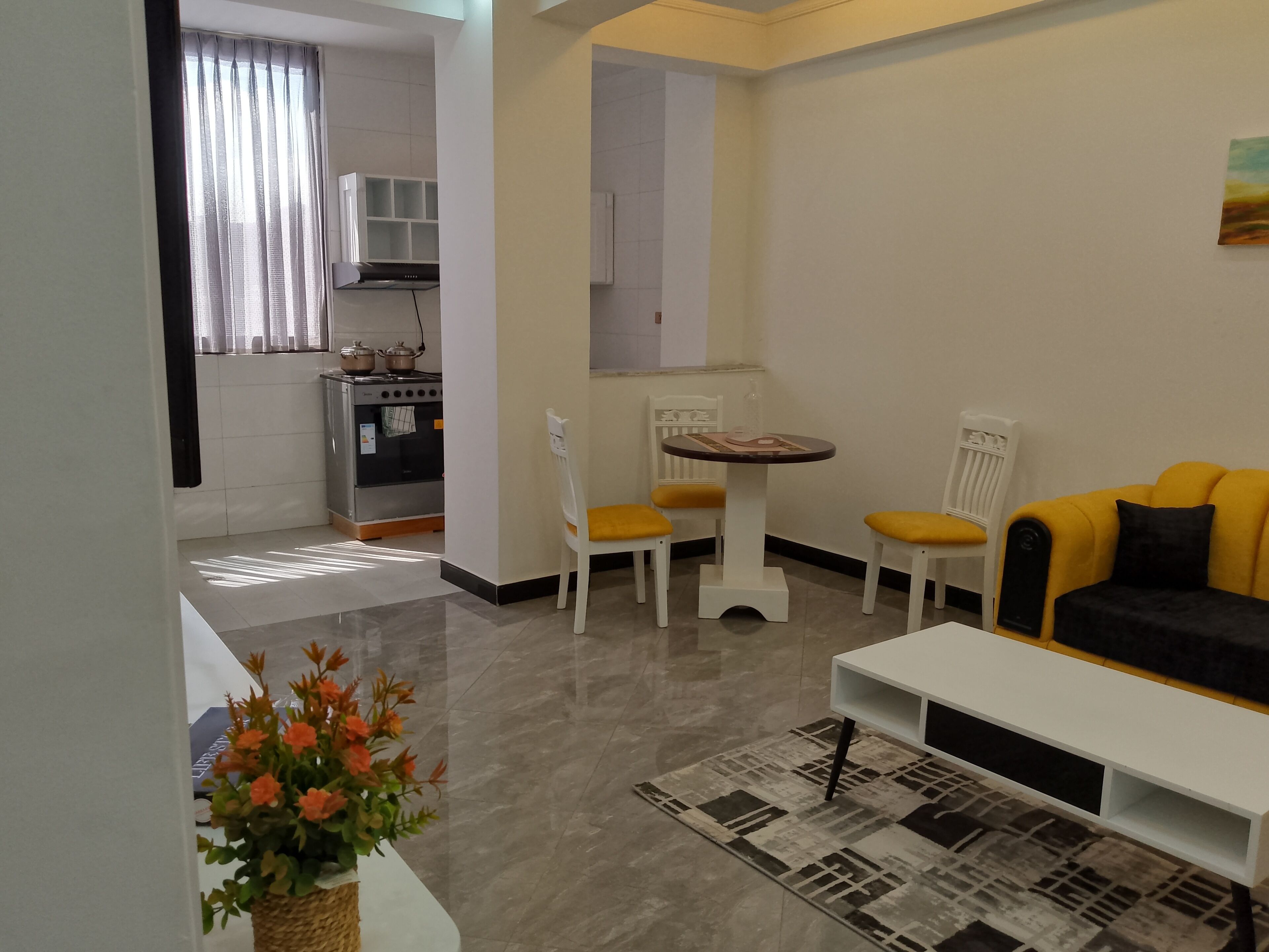 A modern living room with a sofa, chairs, a coffee table, and a kitchen area with an oven and cabinets.