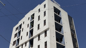 Un hôtel à plusieurs étages au design moderne, doté de balcons à chaque niveau et d’un restaurant situé au rez-de-chaussée.