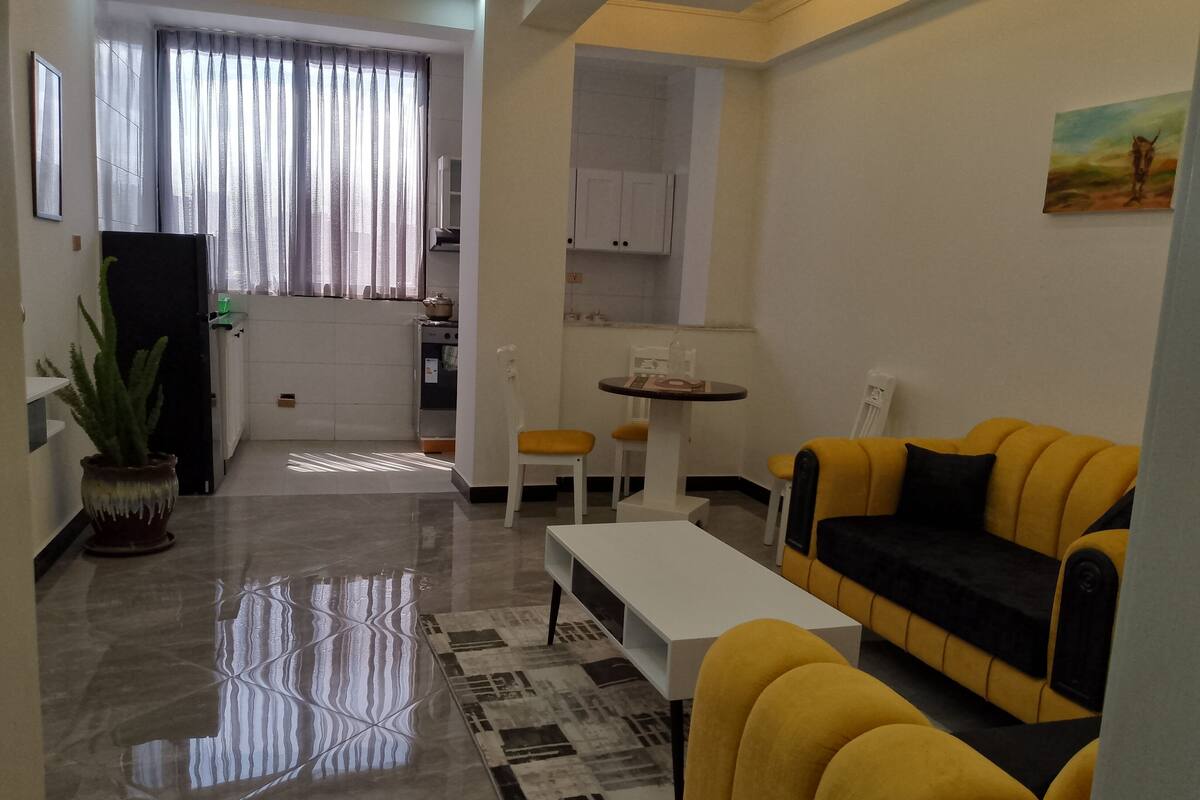 A living room with a yellow sofa, a white coffee table, and a dining area with a small table and chairs.