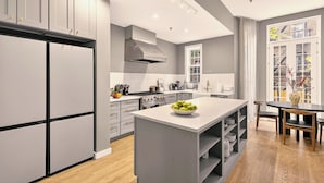 A modern kitchen with grey cabinetry, a central island with a bowl of fruit, and a dining area with a table and chairs. - Outsite Chelsea - Work, Connect, Explore (New York)