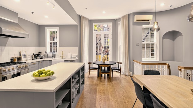 A modern kitchen with a central island, a dining area with a round table, and a view of the outside through large windows. - Outsite Chelsea - Work, Connect, Explore (New York)