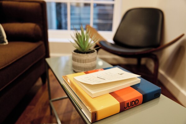 A brown leather sofa, a small potted plant, a black office chair, and a table with books and a document. - Outsite Chelsea - Work, Connect, Explore (New York)