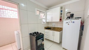 Une cuisine de taille réduite, avec des meubles blancs, une cuisinière à gaz, un évier et un réfrigérateur.