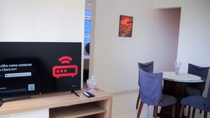 Un salon avec un téléviseur à écran plat affichant un symbole Wi-Fi, un vase en verre et une petite table avec des chaises.