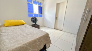 Une chambre à coucher avec un lit, un ventilateur sur pied, une fenêtre et une porte.