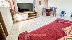 Un salon moderne doté d’un téléviseur à écran plat, d’un coin repas avec des chaises et d’un lit recouvert d’une couverture rouge.