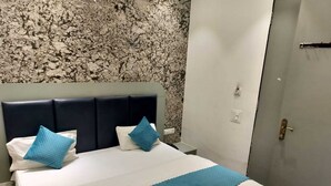 A hotel room with a bed, a headboard, and a door. - Shri Balaji Dham Hotel (Vrindavan)
