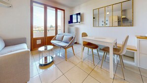 A modern living room with a sofa, a dining table with chairs, a TV, and a large mirror.