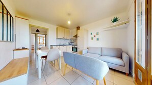 A modern kitchen with white cabinets, a dining area with a white table and chairs, and a grey sofa in a bright living space.