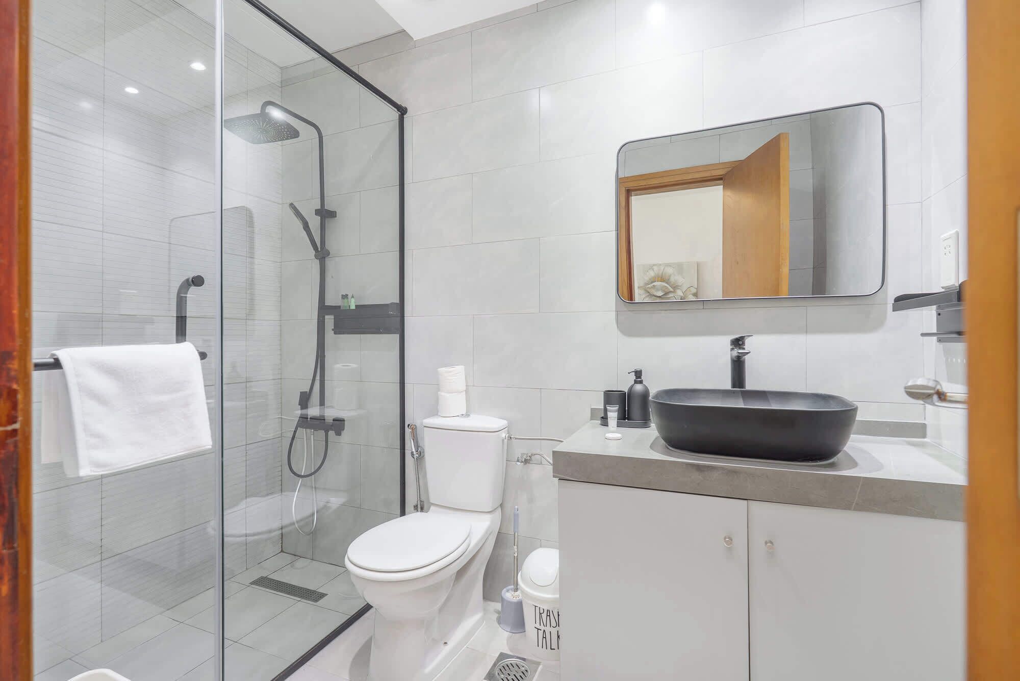 A modern bathroom with a glass-enclosed shower, a white toilet, a black sink, and a mirror above the sink.