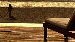 Une terrasse en bois avec un fauteuil de relaxation donnant sur une plage au coucher du soleil.