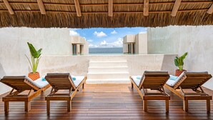 Une terrasse en bois avec des chaises longues et des plantes en pot, offrant une vue sur une piscine et l’océan.
