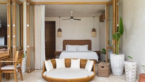 Une chambre spacieuse avec un grand lit, un canapé rond en osier et un coin repas avec des meubles en bois.