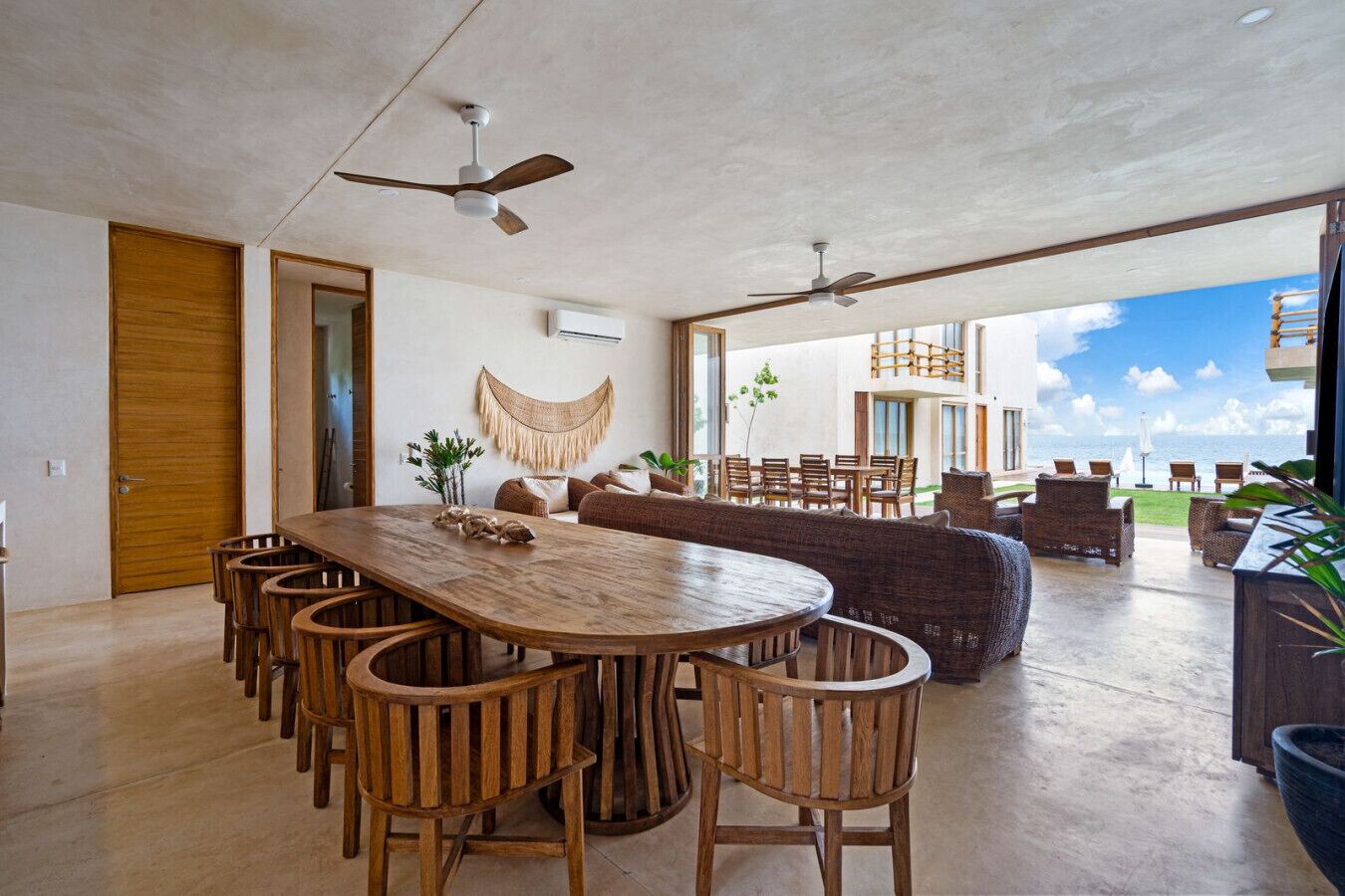 Ein geräumiger Wohnbereich mit einem großen Holzesstisch, umgeben von Stühlen, einer Couch und einem Balkon mit schöner Aussicht.