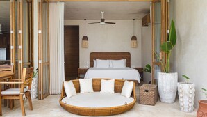 Une chambre à coucher comprenant un lit, un canapé rond en osier, une table à manger, des chaises et un ventilateur de plafond.