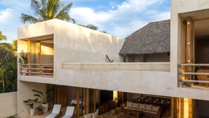 Une villa moderne à plusieurs niveaux, dotée d’un balcon, d’un espace salon extérieur et d’une structure à toit de chaume.