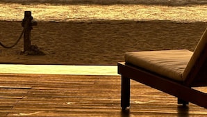 Une terrasse en bois avec un seul fauteuil de relaxation, donnant sur une plage au coucher du soleil.