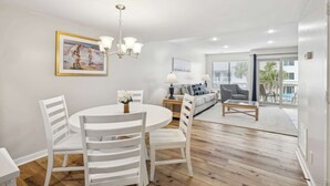 A modern living room with a dining area, a chandelier, and a large window with a view. - Charming Condo Overlooking Pool, Minutes to Beach! (Hilton Head Island)
