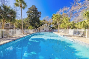 Piscina cercada por um muro branco, palmeiras e um edifício ao fundo.