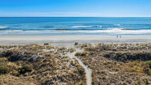 A beach with a clear sky, a sandy path leading to the water, and a few structures in the distance. - Charming Condo Overlooking Pool, Minutes to Beach! (Hilton Head Island)
