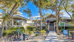 A building with a Real Estate Center sign, a restaurant named FLATBREAD, and a parking area with bicycles. - Charming Condo Overlooking Pool, Minutes to Beach! (Hilton Head Island)