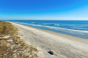 Uma praia com céu claro, areal arenoso e uma pequena construção.