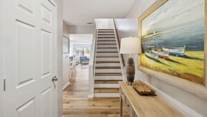 A staircase leading to a second floor, a wooden console table with a lamp, and a painting of boats on water. - Charming Condo Overlooking Pool, Minutes to Beach! (Hilton Head Island)