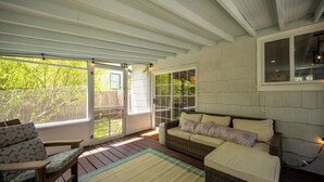 A covered patio area with wicker furniture, a wooden floor, and a view of a backyard.