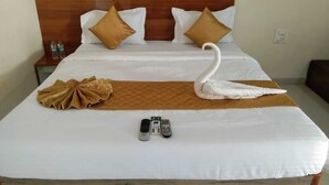 A neatly made bed with a swan-shaped pillow, a brown towel, and two remote controls on the bed. - Atithi Farm House (Kashid)