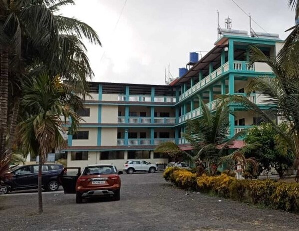 A multi-story building with a central courtyard, surrounded by parked cars and palm trees. - Atithi Farm House (Kashid)