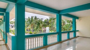 A spacious indoor area with teal-colored columns and a balcony overlooking a garden with palm trees. - Atithi Farm House (Kashid)