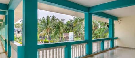 A spacious indoor area with teal-colored columns and a balcony overlooking a garden with palm trees.