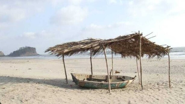 A beach with a thatched-roof structure and a small boat. - Atithi Farm House (Kashid)