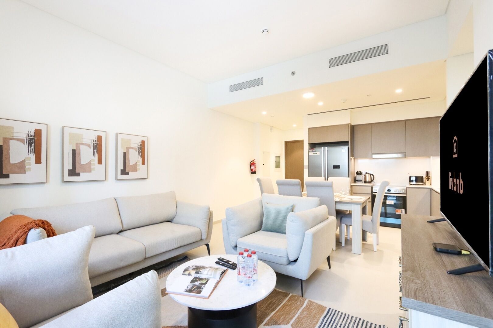 Un salon moderne comprenant un canapé, des fauteuils, une table basse et un coin repas, avec une cuisine en arrière-plan.
