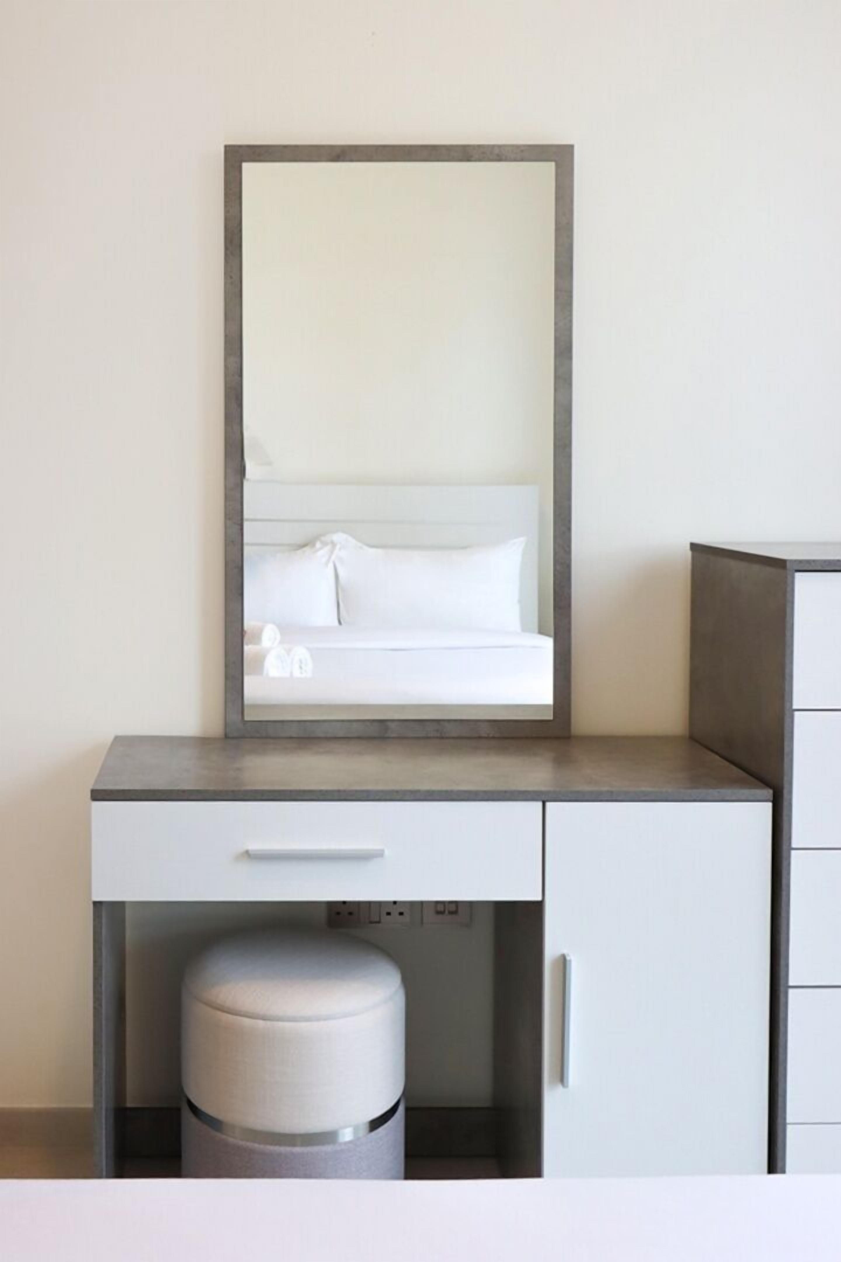 Een moderne hotelkamer met een grote spiegel, een bed met witte lakens, een klein nachtkastje en een afvalbak.